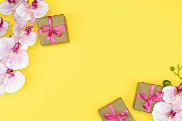 A colocação lisa de caixas do presente do presente com fita rosa no fundo amarelo com flor do orchid. conceito de primavera. Espaço de cópia — Fotografia de Stock