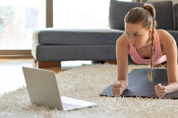 Online sport fitness yoga training. young woman and doing exercises on yoga mat opposite laptop with online master class. training at home