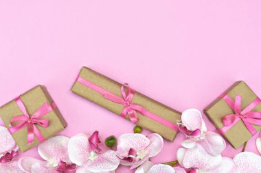 Pembe arka planda pembe kurdeleli hediye kutuları ve orkide çiçeklerinin üst görüntüsü. Hediye ya da şimdiki bahar konsepti. Boşluğu kopyala
