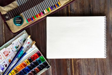 Sanat eserleri, kalemler, fırçalar, suluboya boyalar, kağıt ve pastel tebeşirler. Tahta masanın üzerinde yatıyordu..