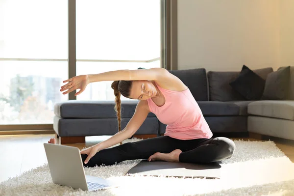 Online sport fitness yoga training. young woman and doing exercises on yoga mat opposite laptop with online master class. training at home