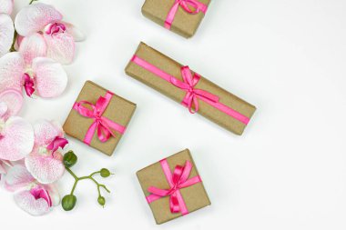 Hediye paketleri pembe kurdeleli, beyaz arkaplanlı orkide çiçekleri. bahar konsepti. Boşluğu kopyala