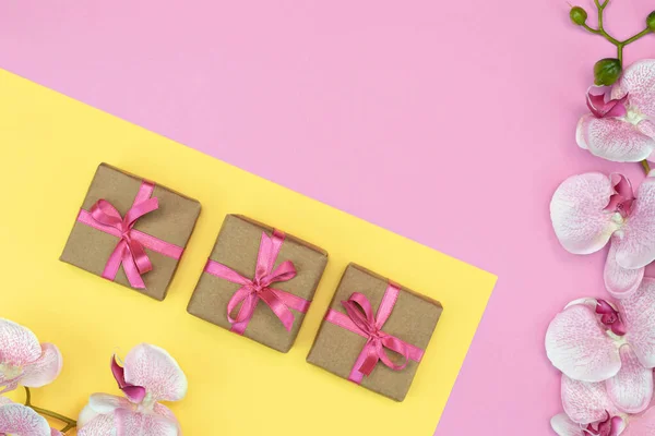 礼物盒的平铺，盒子上有粉色缎带，兰花在粉红色的黄色背景上。春天的概念。复制空间 — 图库照片