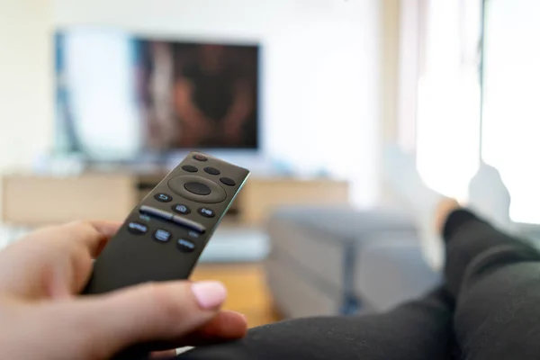 Watching TV, hand holding remote controller in front of big television.