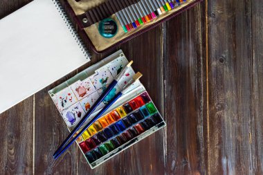 Sanat eserleri, renkli kalemler, fırçalar, suluboya boyalar, kanva kağıtları. Tahta masanın üzerinde düz yatıyordu. Boşluğu kopyala