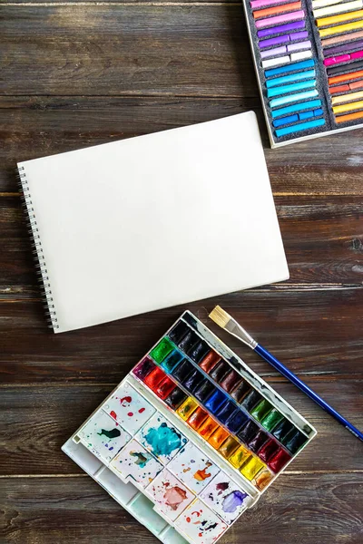 Lugar de trabajo de arte laico plano, mesa de madera con pinceles, pinturas de acuarela, lienzo de papel y lápices de colores pastel — Foto de Stock