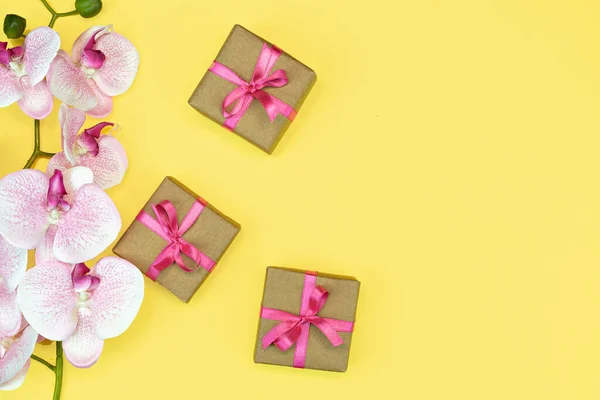 送礼盒的平铺 盒子上有粉色缎带 黄色背景顶部有兰花 礼物或礼物春天的概念 复制空间 — 图库照片