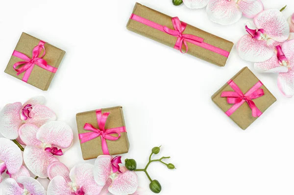 Regalo regalo cajas con cinta rosa, flores de orquídea sobre fondo blanco. concepto de primavera. Copiar espacio — Foto de Stock