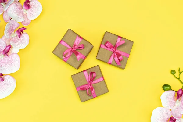 Presente presente caixas com fita rosa, flores de orquídea no fundo amarelo. Espaço de cópia — Fotografia de Stock
