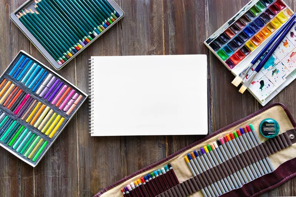 Arte lugar de trabajo, lápices, pinceles, pinturas de acuarela, papel y lápices de colores pastel. Colocación plana sobre mesa de madera — Foto de Stock