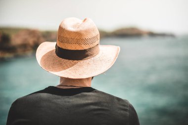 Şapkalı bekar erkek su ve kayalıklarla uzaklara bakıyor.