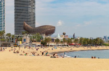 Barcelona 'daki şehir plajı, insanlar plajda dinleniyor, arka planda Peix Olimpik Frank Gehry. İspanya, Barselona Mayıs 2019