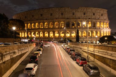 View of the night Colosseum, the road with passing cars. Rome, Italy.