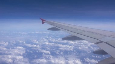 Bulutların üzerinde uçan bir uçağın kanadı, yolcu koltuğundaki uçağın penceresinden görünen manzara..