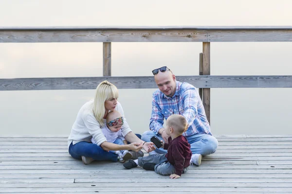 Heureux famille de deux parents et enfants, un garçon, petite fille, assis ensemble sur la jetée de la rivière . — Photo