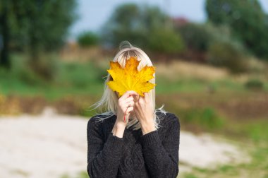 Gülümseyen sarışın sonbahar büyük akçaağaç yaprağı çehresini kapatır