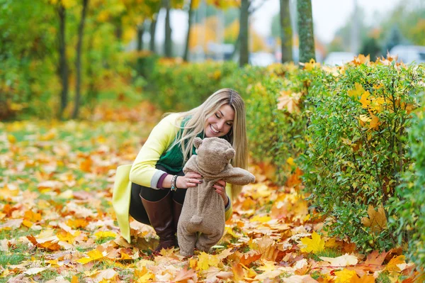 The beautiful woman in the autumn park holding teddy bear — Stock Photo, Image