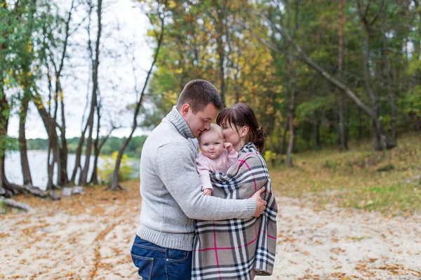 Portrait of happy couple embracing her little daughter over a forest background. — Stock Photo, Image