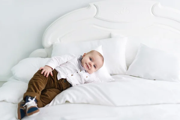 De charmante en rustige jongen in kleding ligt op witte deken in slaapkamer — Stockfoto