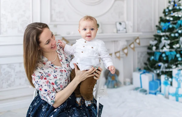 Retrato de madre feliz y adorable bebé contra el telón de fondo festivo doméstico con árbol de Navidad — Foto de Stock