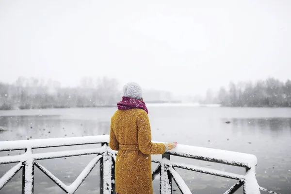 Young woman stands near a frozen lake.