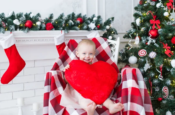 Niña con gran corazón rojo se sienta en una silla cerca del árbol de Navidad — Foto de Stock