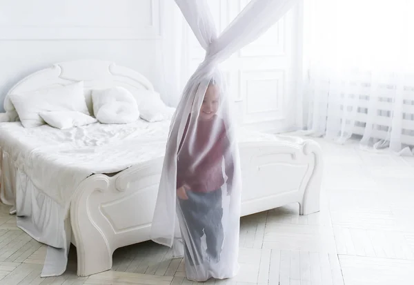 O menino se escondeu para uma cortina em um grande quarto leve . — Fotografia de Stock