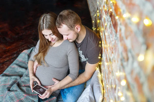 Vista superior do jovem casal sentado no chão, esperando por um bebê. Consideram a foto ultrassonografia . — Fotografia de Stock