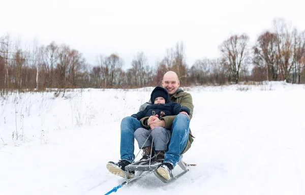 Jeune homme avec le petit garçon assis sur un traîneau dans la neige — Photo