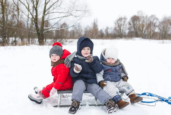 Trois enfants s'assoient sur la luge le jour d'hiver . — Photo