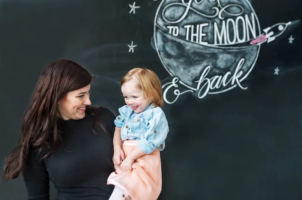 Portrait of young mother with little daughter against the background of ornamented wall. — Stock Photo, Image