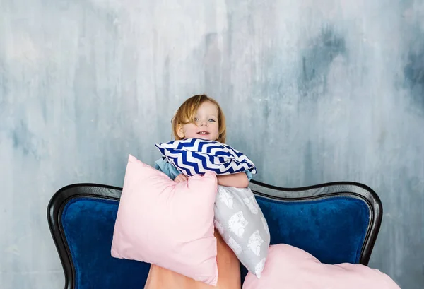 Das charmante Kind steht auf dem Sofa mit Kissen in den Händen. — Stockfoto