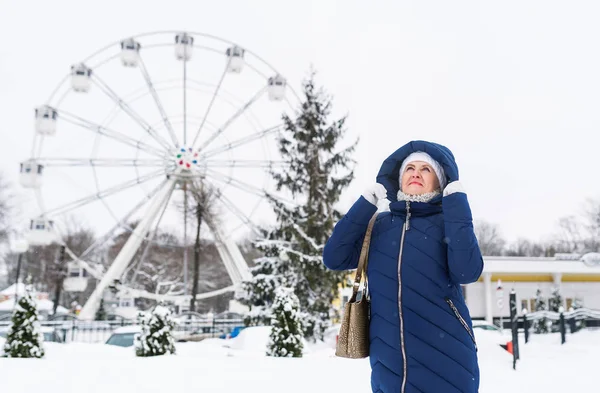 Mulher adulta vestindo casaco com capuz azul desfrutando de passear no parque de diversões de inverno ao ar livre . — Fotografia de Stock