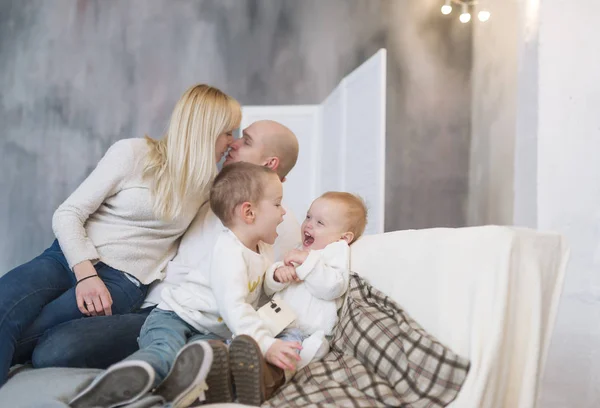 Портрет целующихся родителей и их маленьких детей, сидящих дома на мягком диване . — стоковое фото