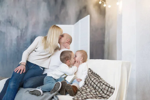 Портрет целующихся родителей и их маленьких детей, сидящих дома на мягком диване . — стоковое фото