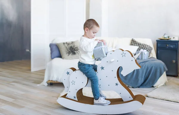 Cute baby boy riding wooden traditional rocking horse toy in white bedroom. Child playing in nursery room. — Stock Photo, Image