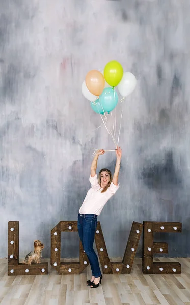 Porträt einer niedlichen jungen Frau, die in einem Atelier steht, breit lächelt und mit bunten Luftballons spielt — Stockfoto