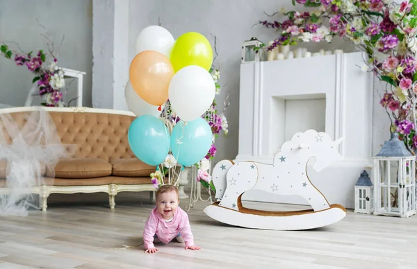 Adorable niña caucásica con globos de colores se arrastra en el suelo de madera en casa — Foto de Stock