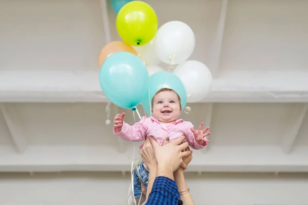 Cute little baby girl turned 6 months old. Baby girl is in hands of parents indoors with balloons on the background — Stock Photo, Image