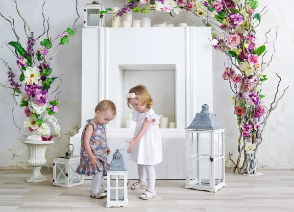 Dos niñas encantadoras juegan en la sala de luz decorada con flores. Niñas y candelabro grande — Foto de Stock