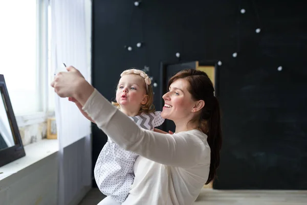 Sonriendo mamá haciendo selfie con su hija bebé en el fondo de la ventana — Foto de Stock