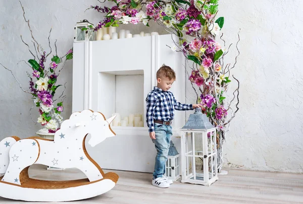 Der schöne Junge in Jeans steht im hellen Atelier, das mit Blumen geschmückt ist. — Stockfoto