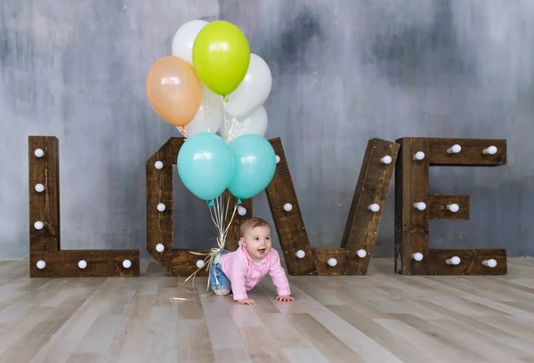Adorable caucasian baby girl with colorfull balloons creeps on wooden floor at studio — Stock Photo, Image