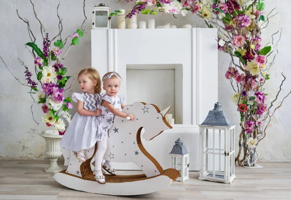 두 매력적인 소녀는 꽃으로 장식 된 라이트 룸에서 재생 합니다. 여자 아기 나무 말에 스윙 — 스톡 사진