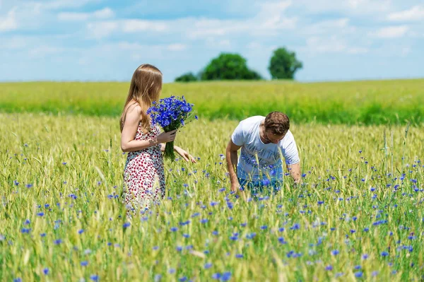 Pareja joven caminando en el campo con flores — Foto de Stock