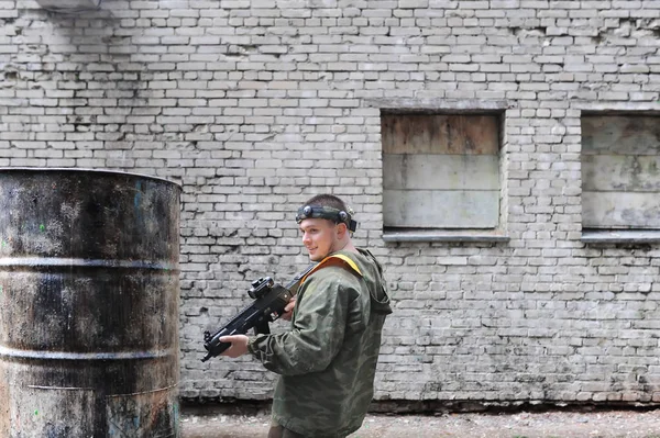 Hombre jugando paintball en overoles con un arma en la fábrica lanzada —  Fotos de Stock