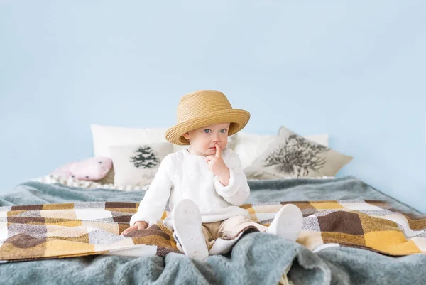 Menina bonita em chapéu de palha com olhos azuis e uma expressão pensativa sentada em sua cama — Fotografia de Stock