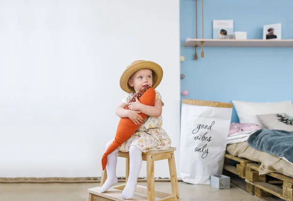 Kleines Mädchen, das auf einem Stuhl sitzt und zu Hause einen Spielzeugfisch hält. — Stockfoto