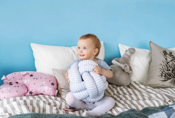 Süßes kleines Mädchen umarmt ein Kissen, schaut Mama an und lächelt, während sie zu Hause auf ihrem Bett sitzt — Stockfoto