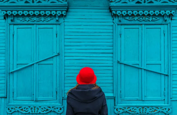 Frau mit roter Mütze blickt auf das blaue alte Dorfhaus in einem russischen Dorf — Stockfoto